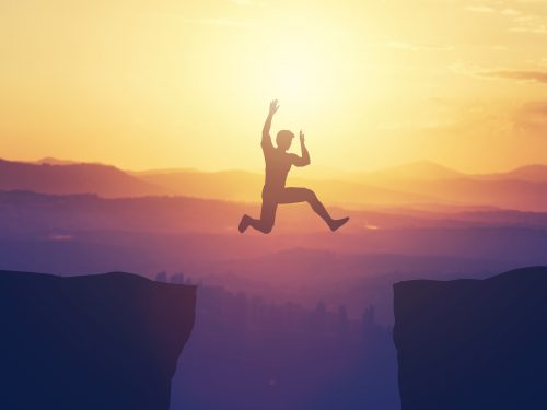 Man jumping above the cliff in the mountains. Risk, danger and challenge. Sunset.